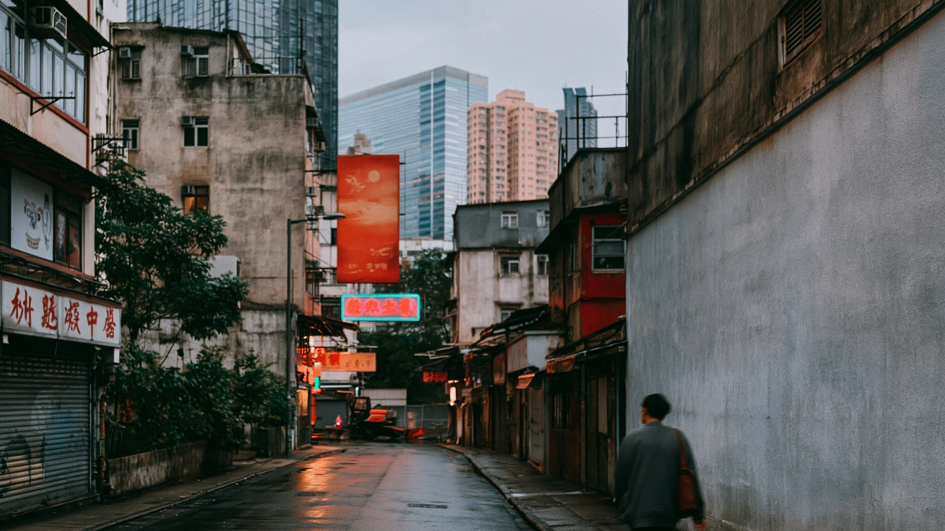 A narrow city street at dusk with red neon signs and a wet road